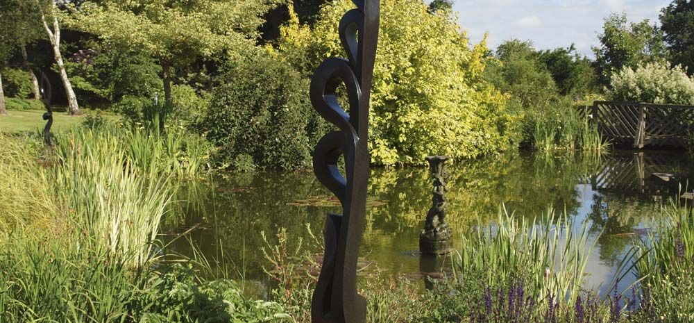 Shona sculpture UK exhibition - unique abstract stone sculpture by a pond
