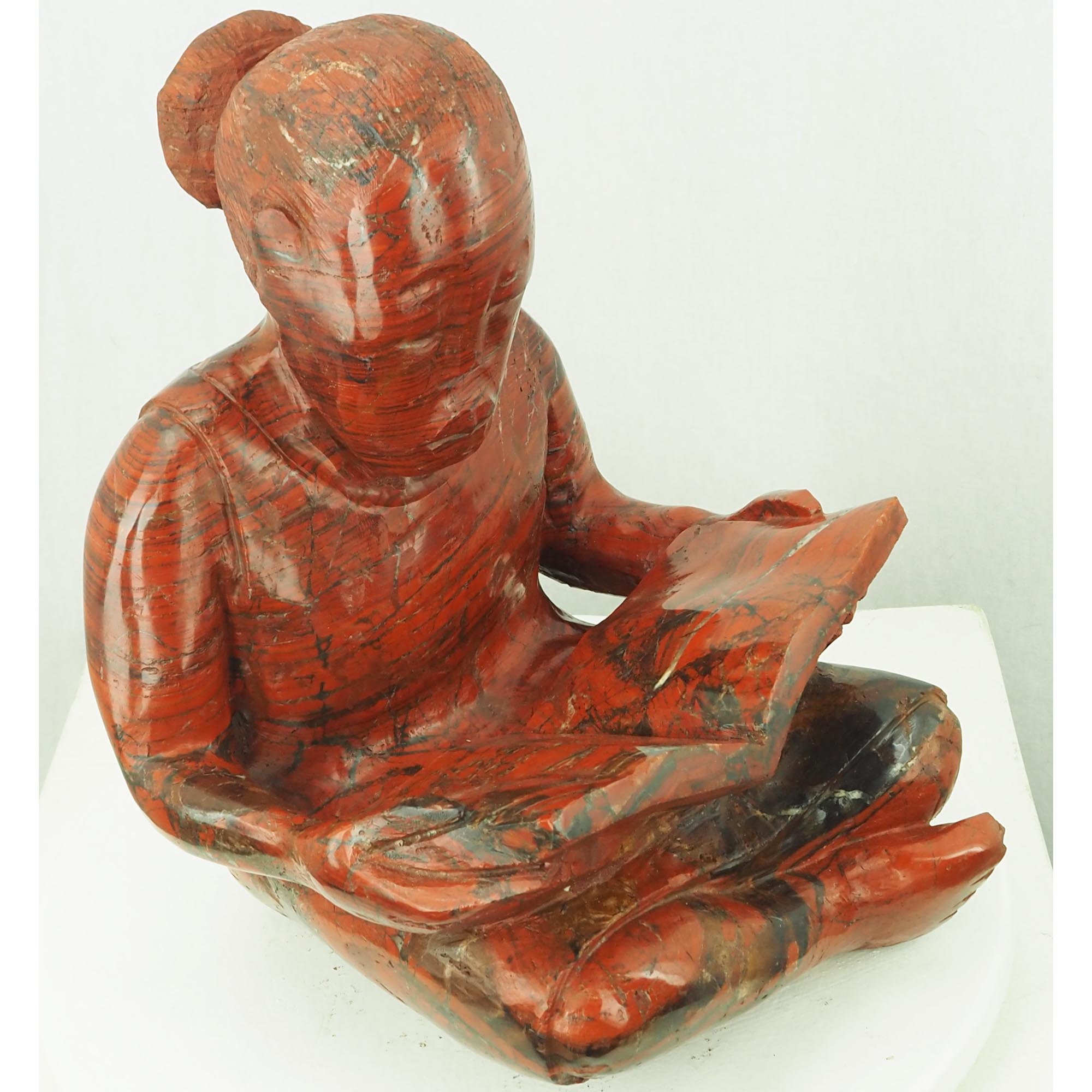 Sculpture child girl reading red stone - Doing My Homework by Jonathan Mhondorohuma - front left from above